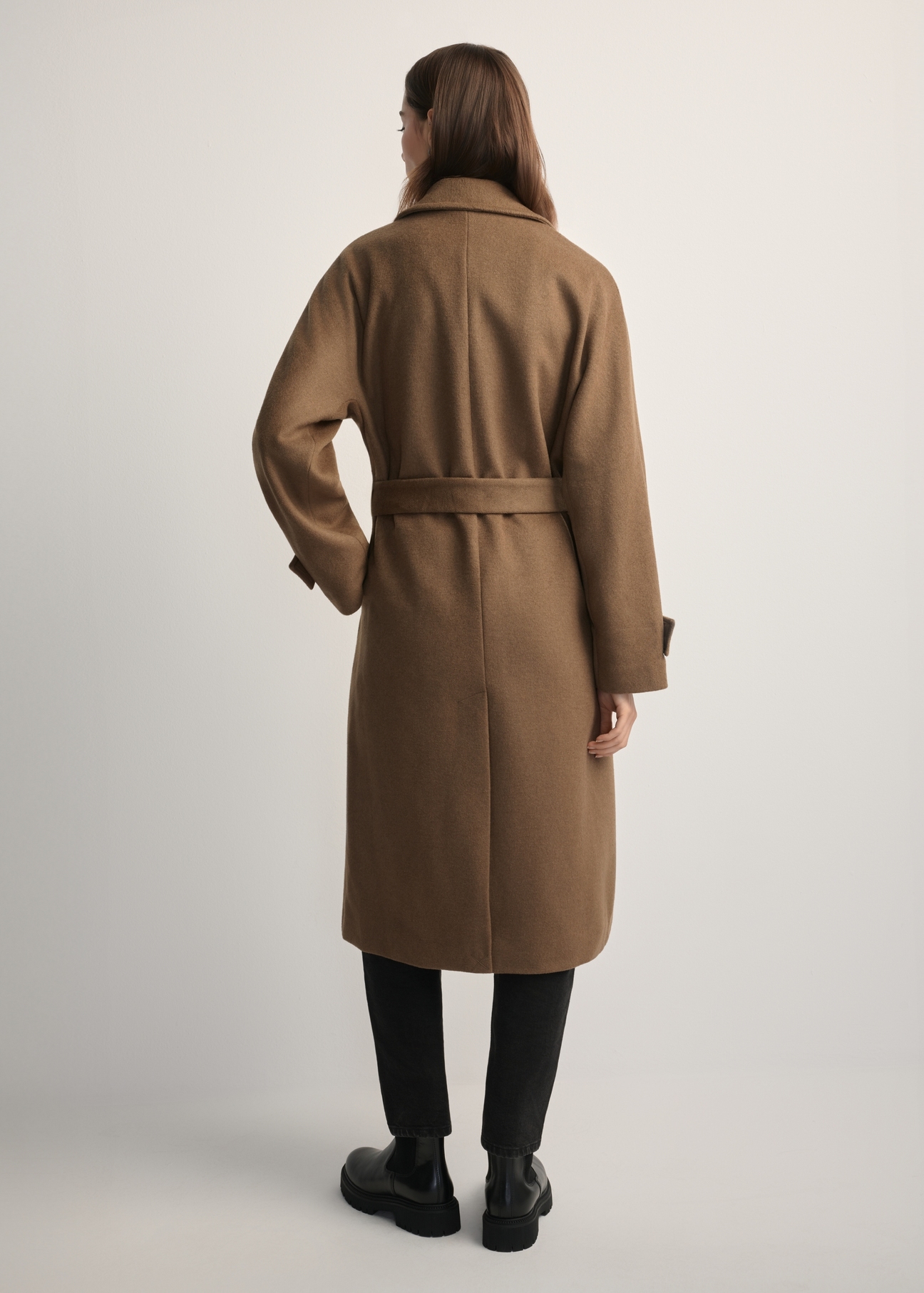 Wełniany płaszcz damski camelowy PLADT-0061-24(Z25) - widok produktu z tyłu, na modelce, na jasnym tle.  Widoczna cała sylwetka.