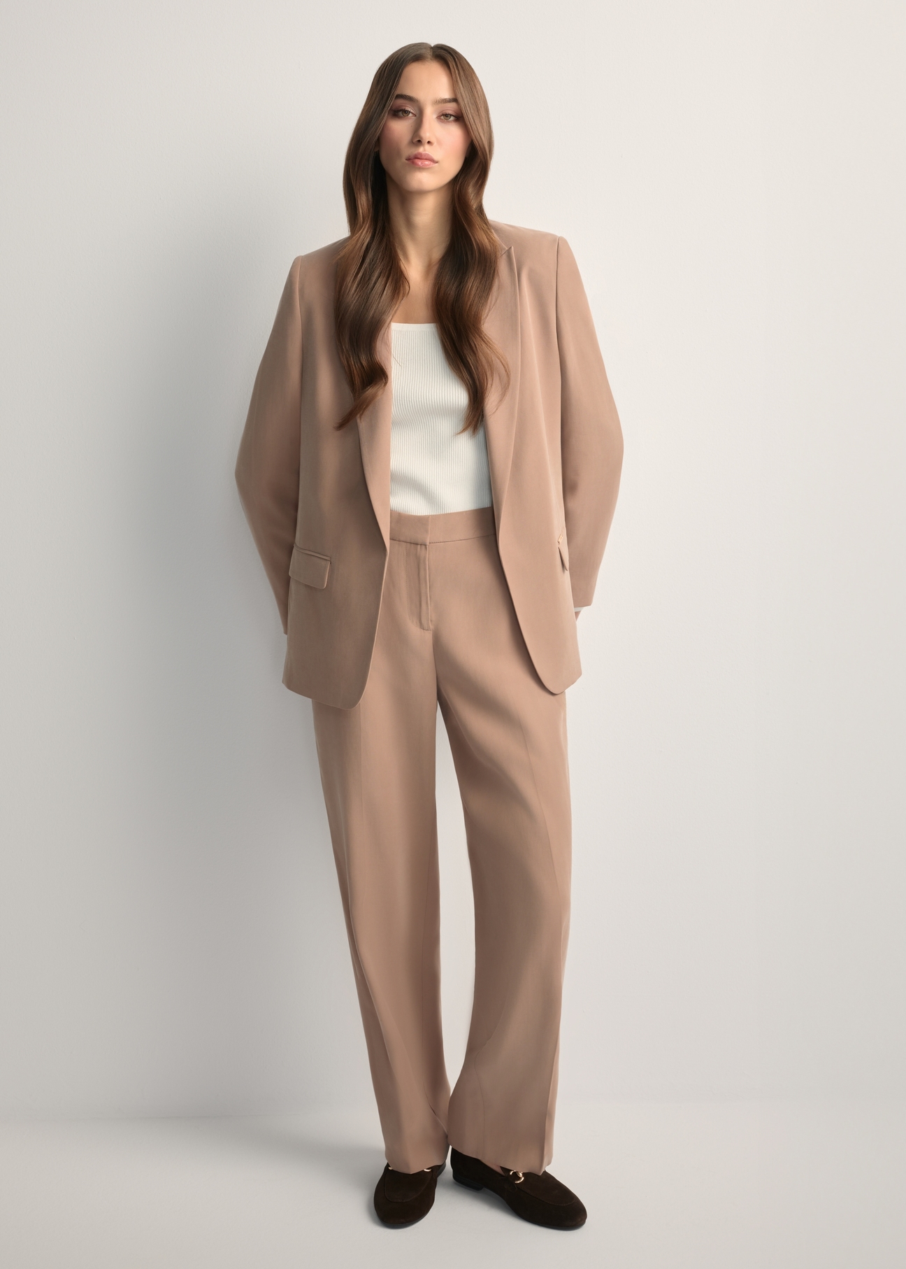 Beżowe eleganckie spodnie damskie SPODT-0106A-1D(W26), widok produktu z przodu na modelce. Widoczna cała sylwetka.