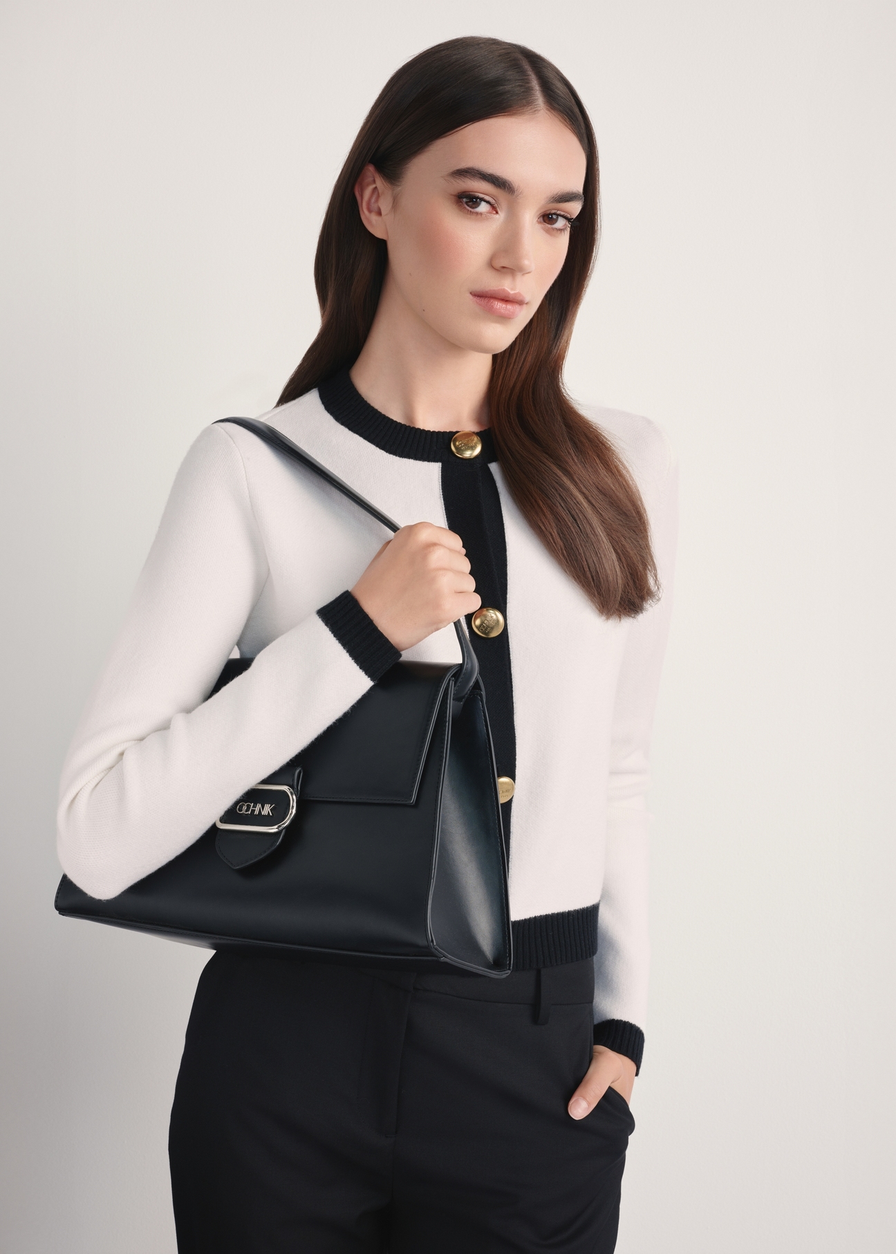 Elegancka czarna torebka damska TOREC-1068-99(Z25) - widok produktu po skosie na modelce, na białym tle. Widoczna połowa sylwetki bokiem.