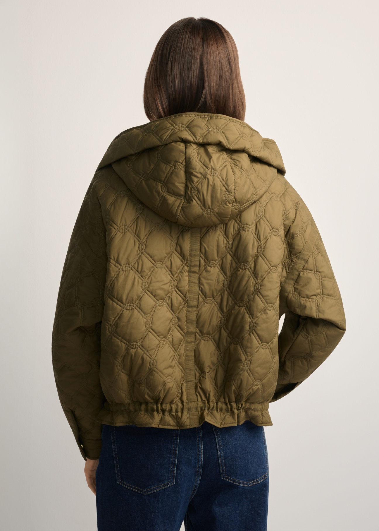 Oliwkowa krótka pikowana kurtka oversize KURDT-0660-8D(W26) - widok produktu z tyłu, na modelce, na jasnym tle. Widoczna połowa sylwetki. 