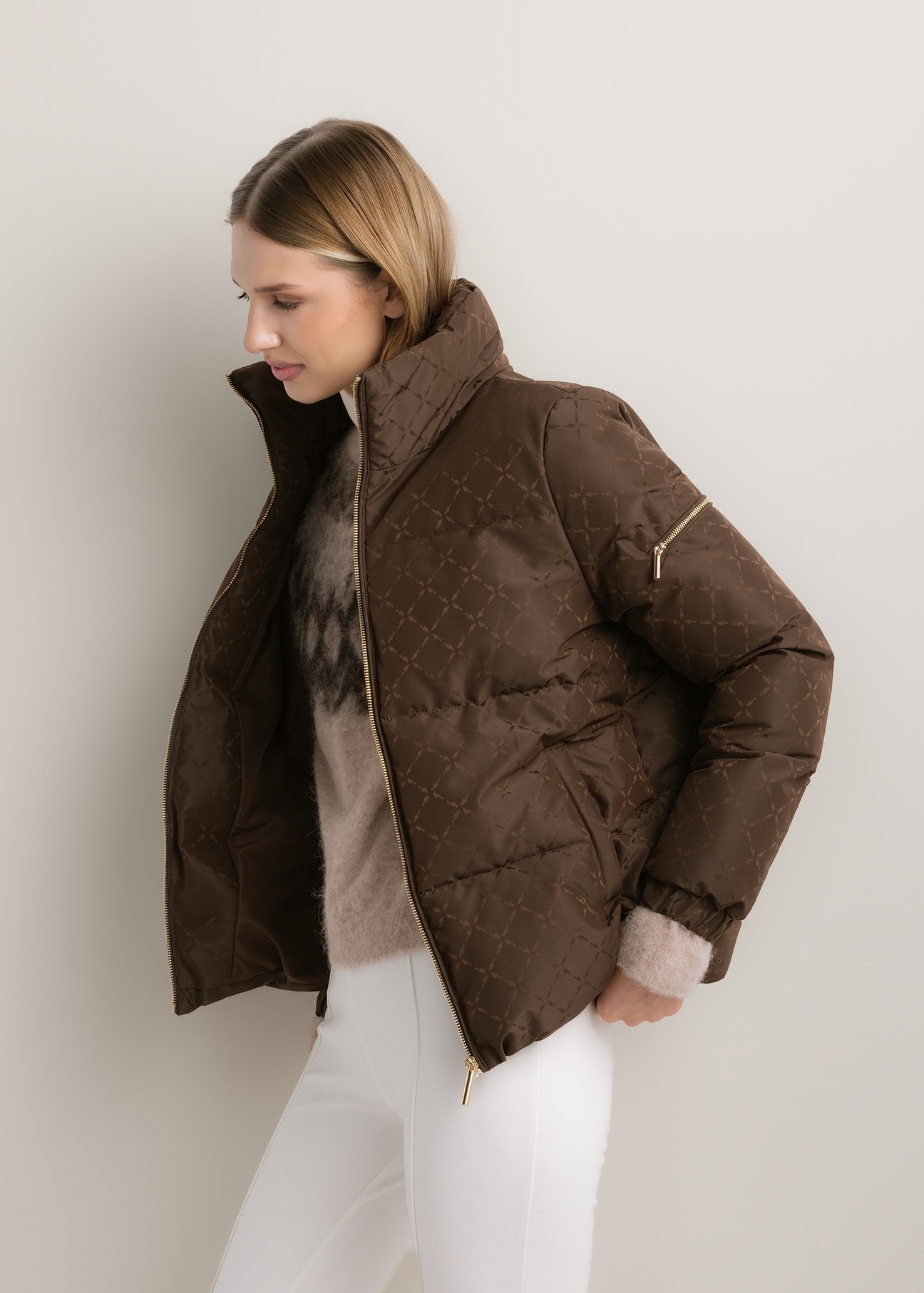 Ciemnobrązowa kurtka damska w monogram ze stójką KURDT-0694-1I(Z26), widok produktu skosem na modelce. Widoczna połowa sylwetki.