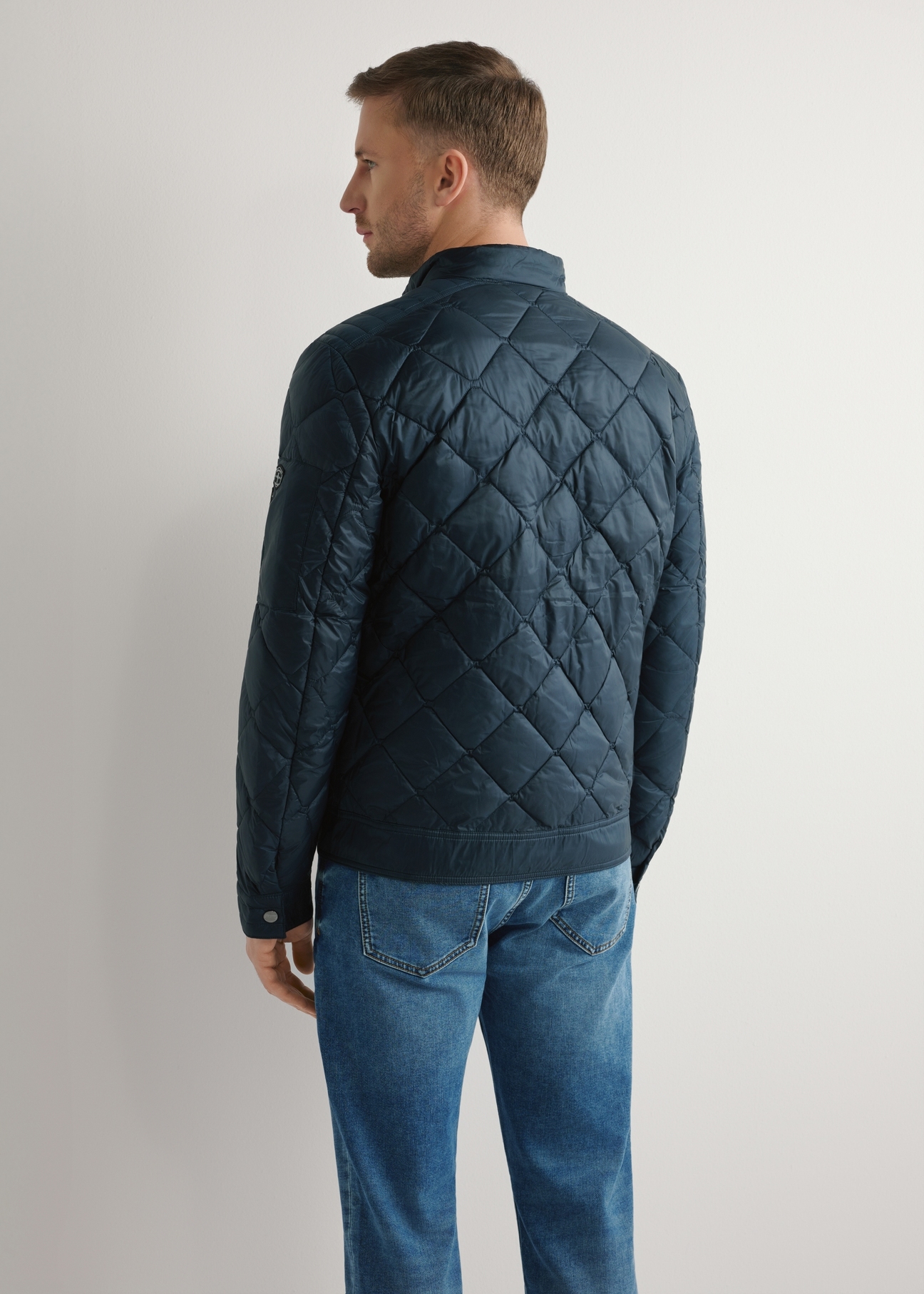 Granatowa kurtka męska pikowana KURMT-0327-7C(W26) - widok produktu z tyłu na modelu, na jasnym tle. Widoczna sylwetka do kolan. 