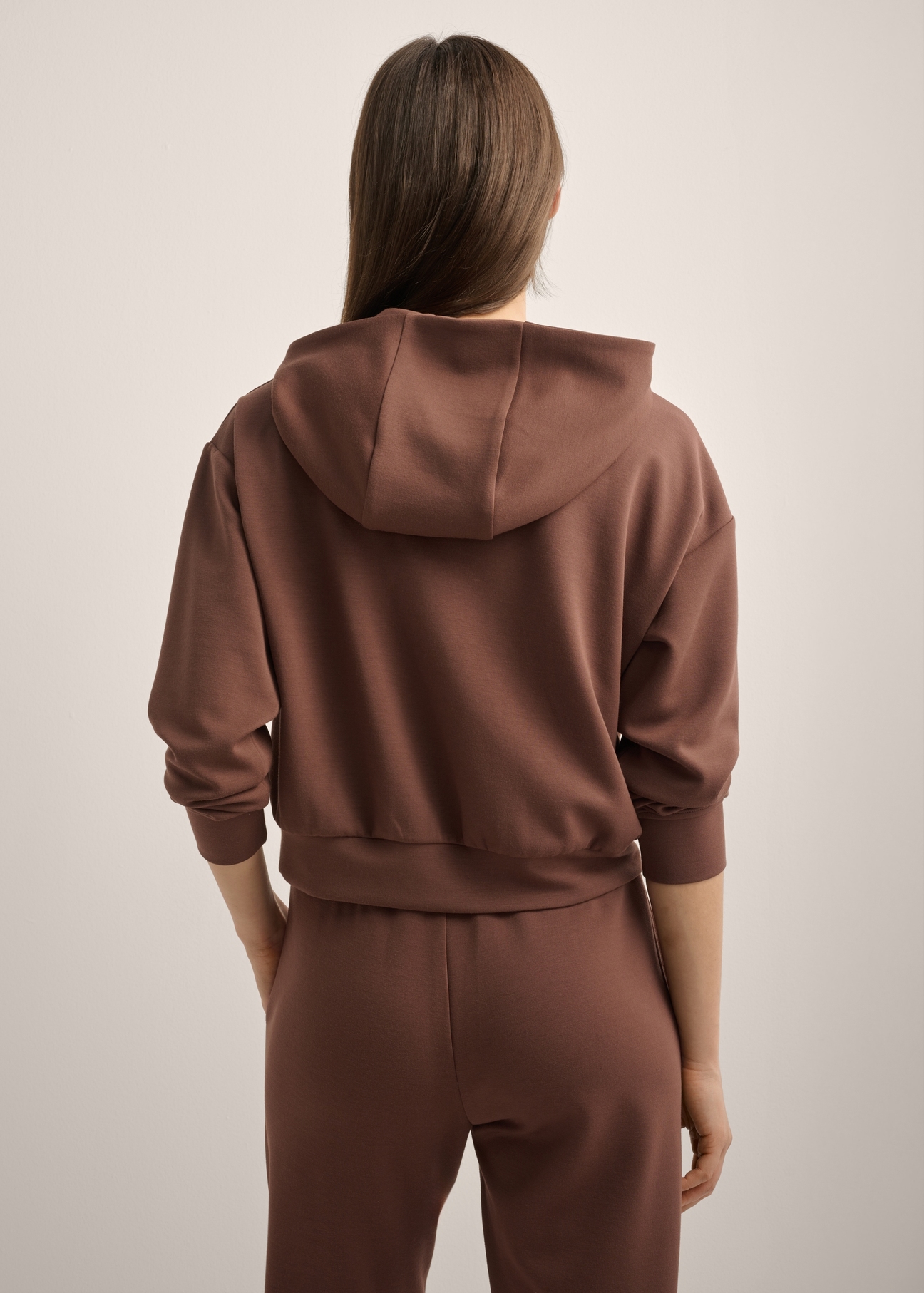 Brązowa bluza damska z kapturem BLZDT-0118-1H(Z26), widok produktu od tyłu na modelce. Widoczna połowa sylwetki.