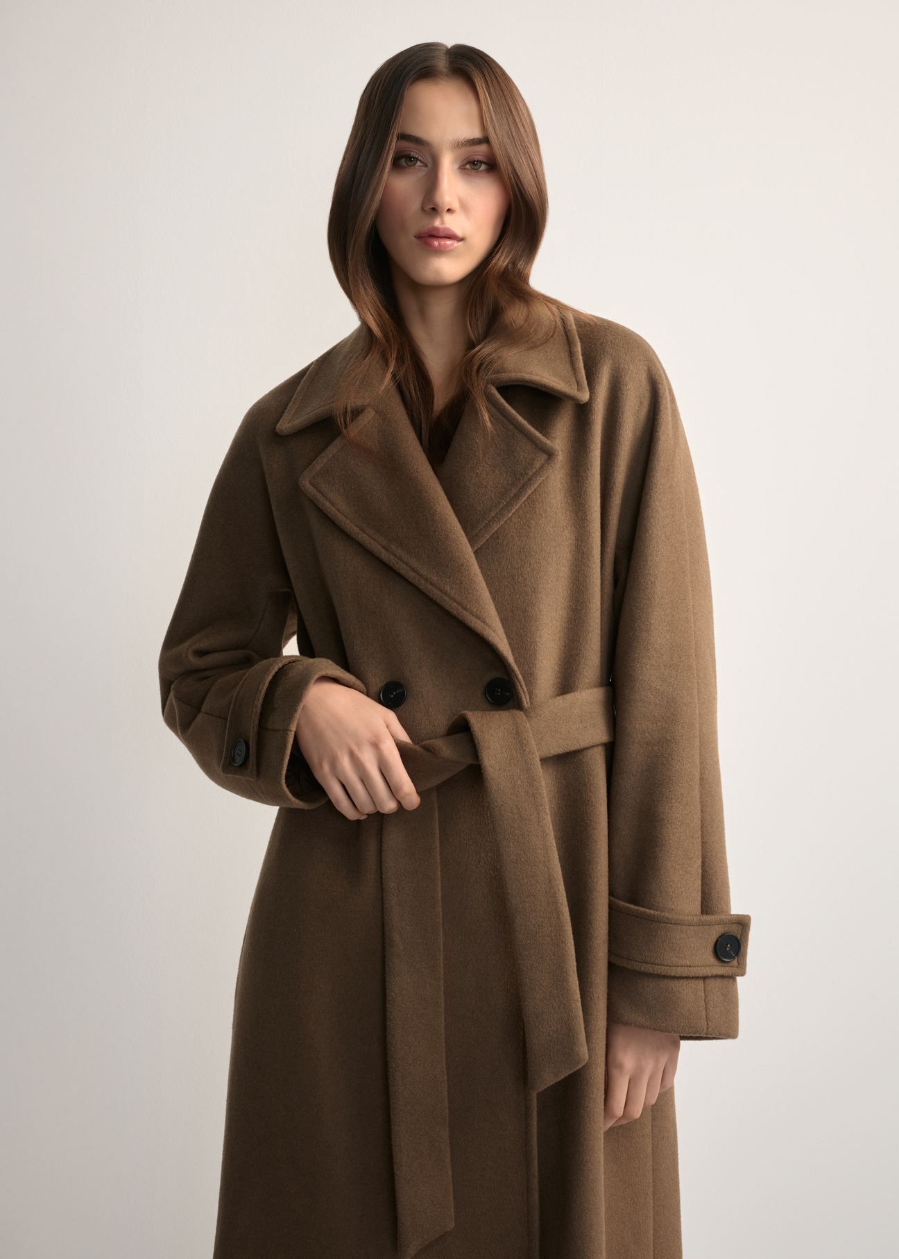 Wełniany płaszcz damski camelowy PLADT-0061-24(Z25) - widok produktu z przodu, na modelce, na jasnym tle. Widoczna połowa sylwetki.