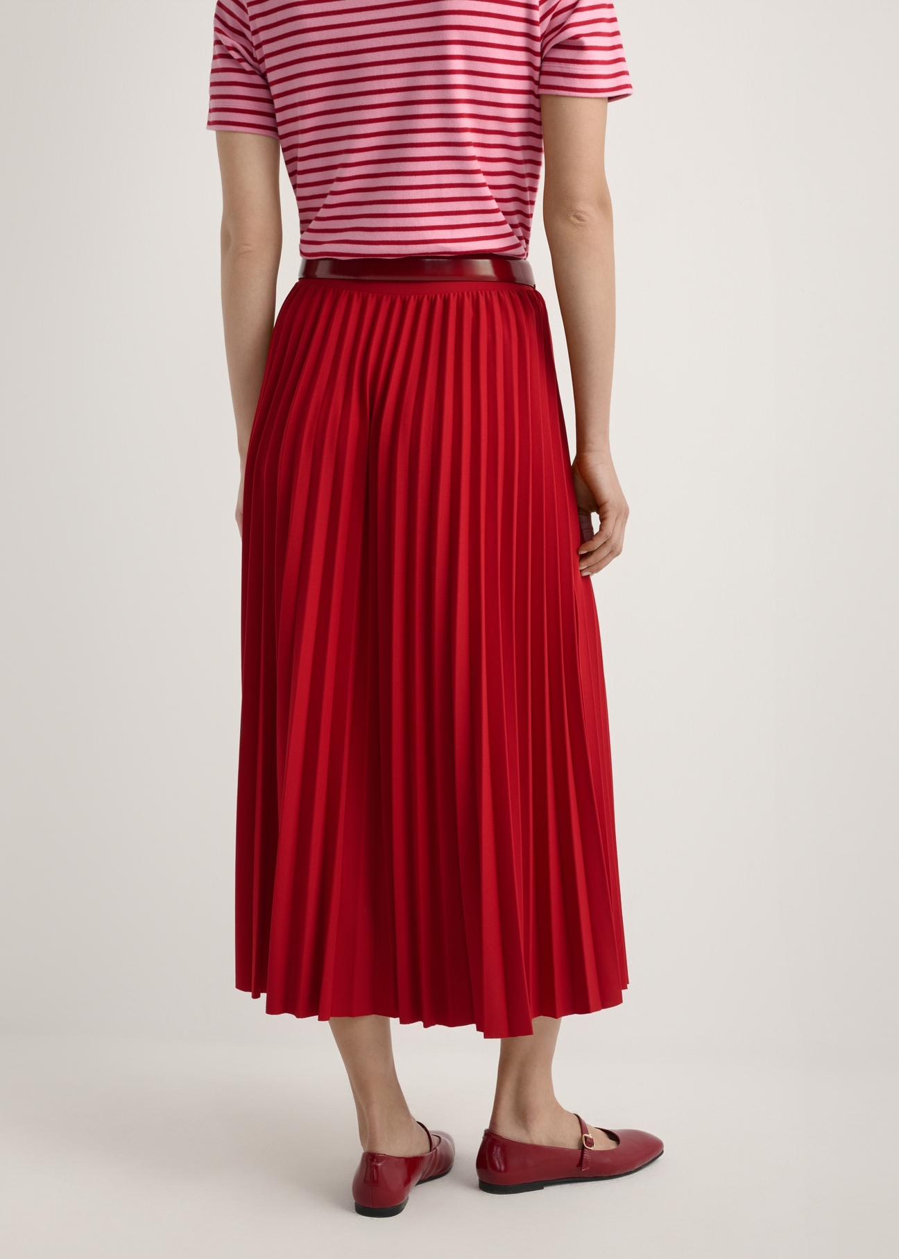 Czerwona plisowana spódnica midi SPCDT-0096-4B(W26), widok produktu od tyłu na modelce, widoczna połowa sylwetki.