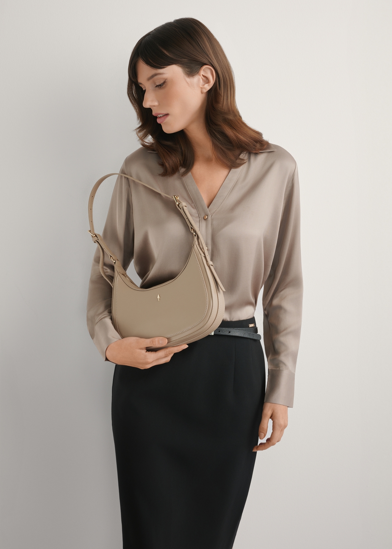 Beżowa mała torebka hobo TOREC-1136-1A(W26), widok produktu w dłoni modelki. Widoczna połowa sylwetki.