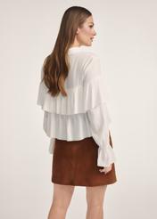 Biała bluzka damska z falbankami BLUDT-0198-12(Z25), widok produktu z tyłu na modelce. Widoczna połowa sylwetki.