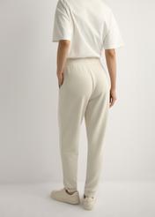 Jasnobeżowe spodnie damskie SPODT-0108-1A(W26), widok produktu z tyłu na modelce. Widoczna połowa sylwetki.