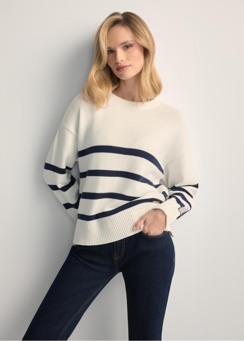 Kremowy sweter damski w paski SWEDT-0258-0B(W26) - widok produktu z przodu, na modelce, na jasnym tle. Widoczna sylwetka do kolan. 